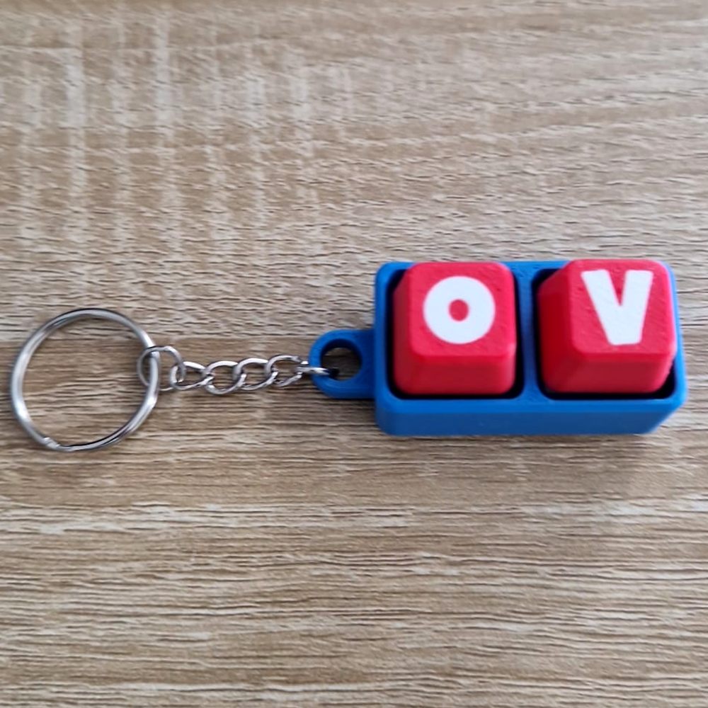 Porte-clés imprimé en 3D façon touches de clavier, lettres O et V blanches sur touches rouges.